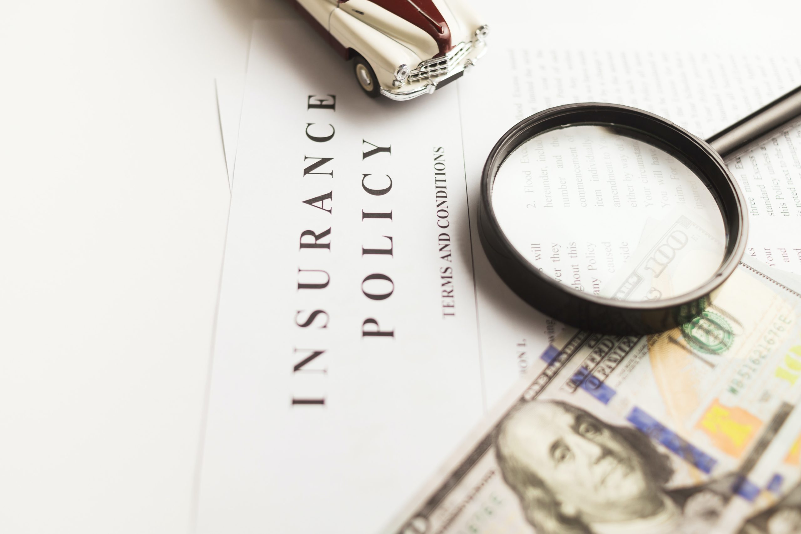 Money, magnifying glass and toy car lying on insurance policy